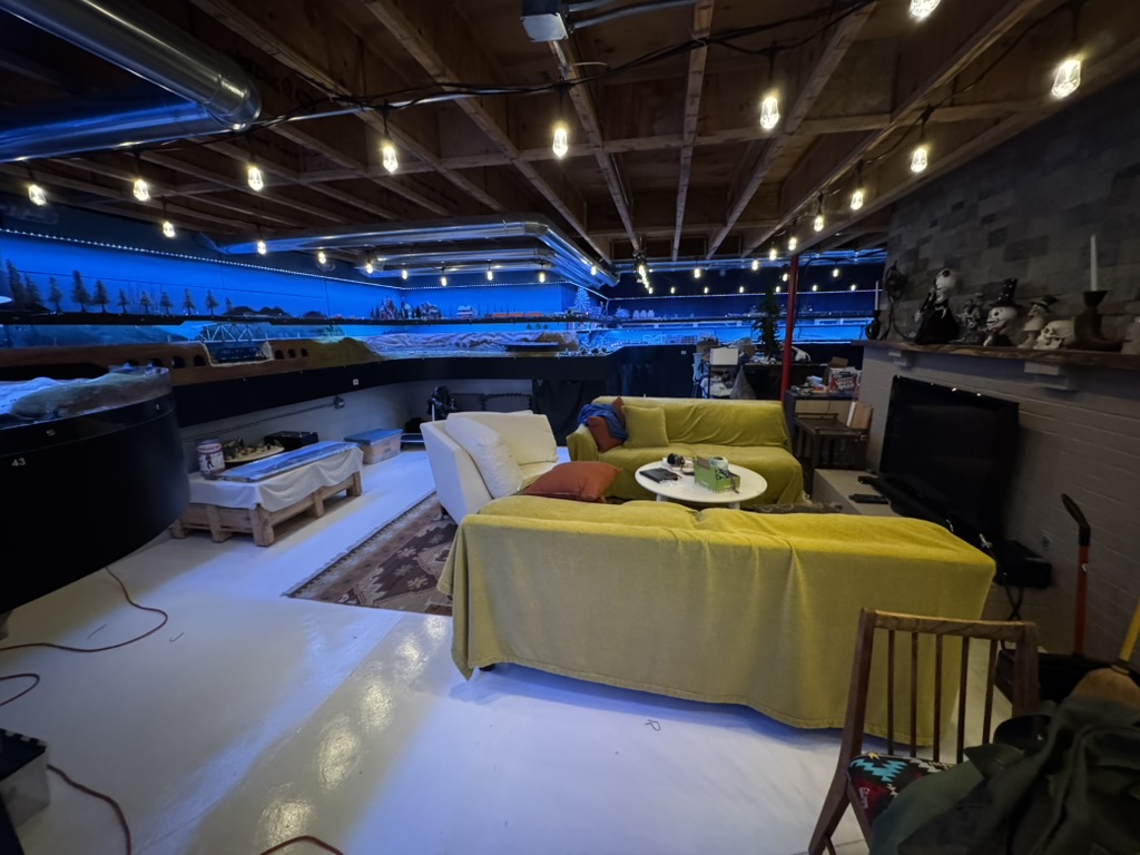 Full model railroad train room with multi-deck layout and lounge seating area.